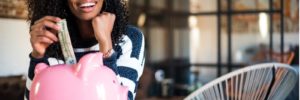 Young woman putting money into a piggy bank and smiling